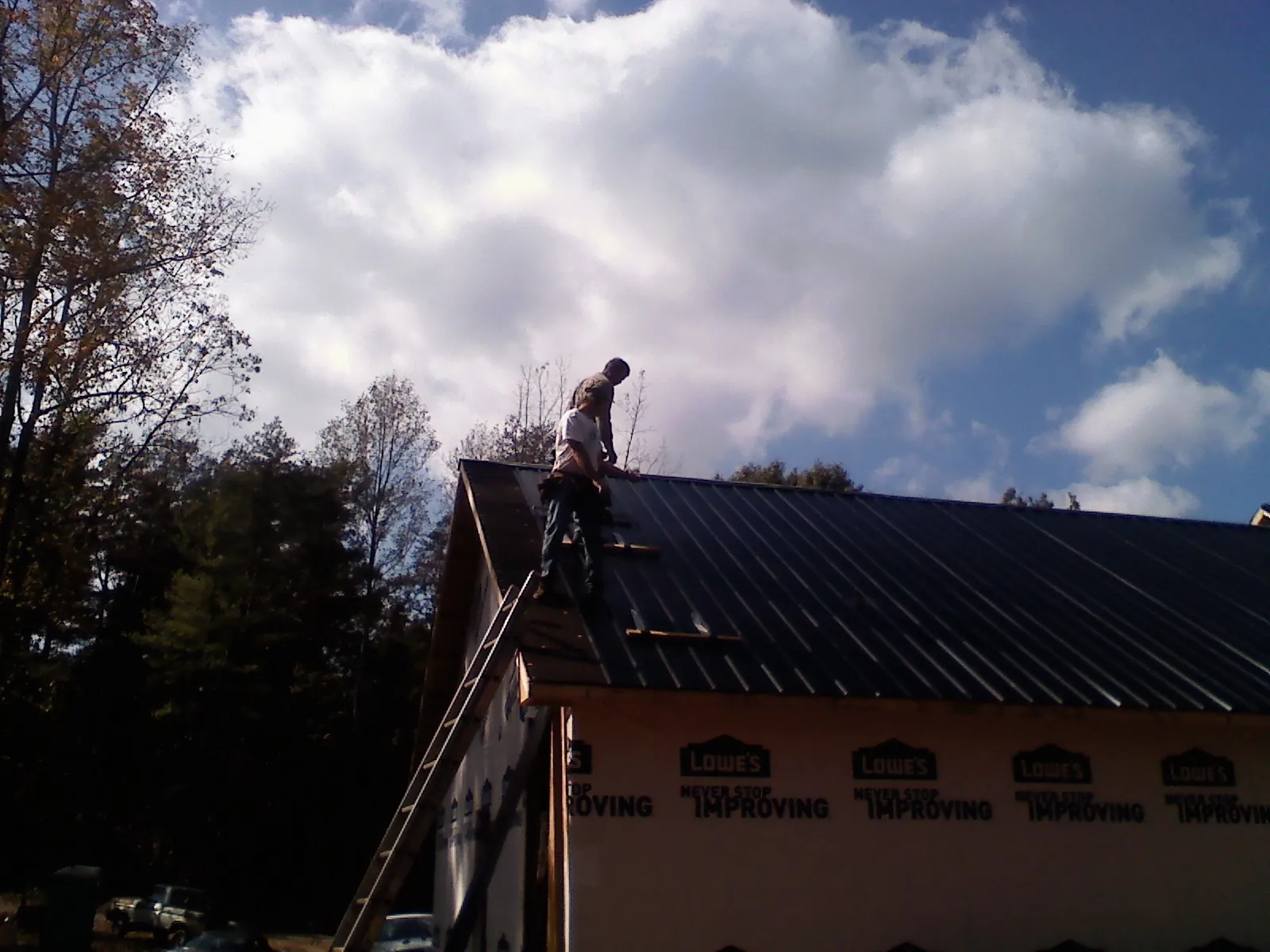 Roofer fastening dark metal panels high against a cloudy sky, from a Roof Inspection job in Marysvale