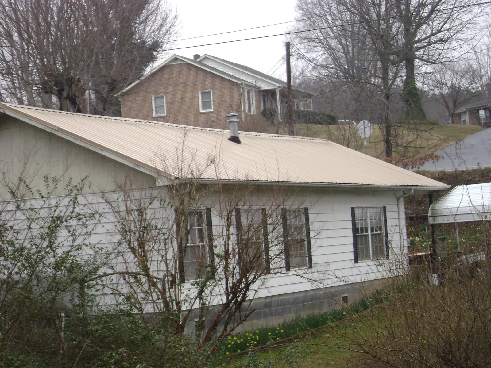 Tan metal roof on a white sided house set into a hillside — Commercial Roofing by Roofing Brothers in Marysvale